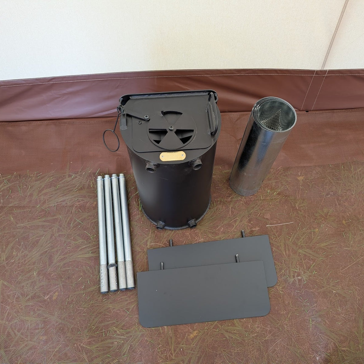 Roamin Home Packer wood-burning tent stove with chimney pipe sections, spark arrestor, and stove components laid out for assembly inside a canvas wall tent. Compact camping wood stove designed to provide warmth during hunting trips and outdoor adventures.