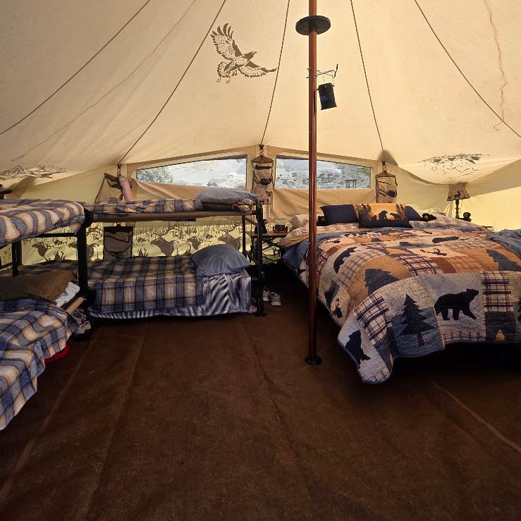 A warm, roomy Roamin Home canvas wall tent set up for a comfortable stay, with 2 full size bunk cots, a cozy queen size bed, 2 end tables, soft bedding, and plenty of open floor space between them.