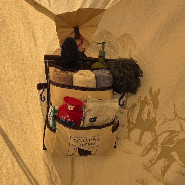 Roamin Home Deluxe Pocket hanging inside a canvas tent, with cream canvas pockets and brown trim holding toiletries, a hairbrush, and other personal items.