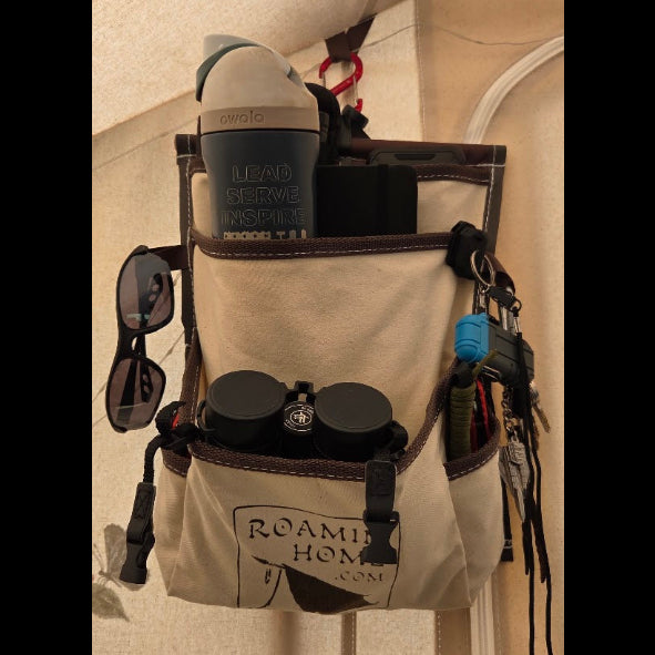 Cream canvas Roamin Home Deluxe Pocket hanging inside a tent, holding a water bottle and binoculars, with sunglasses and keys attached to the sides.